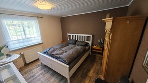 Een slaapkamer met een bed, nachtkastje, dressoir, raam en een radiator.
