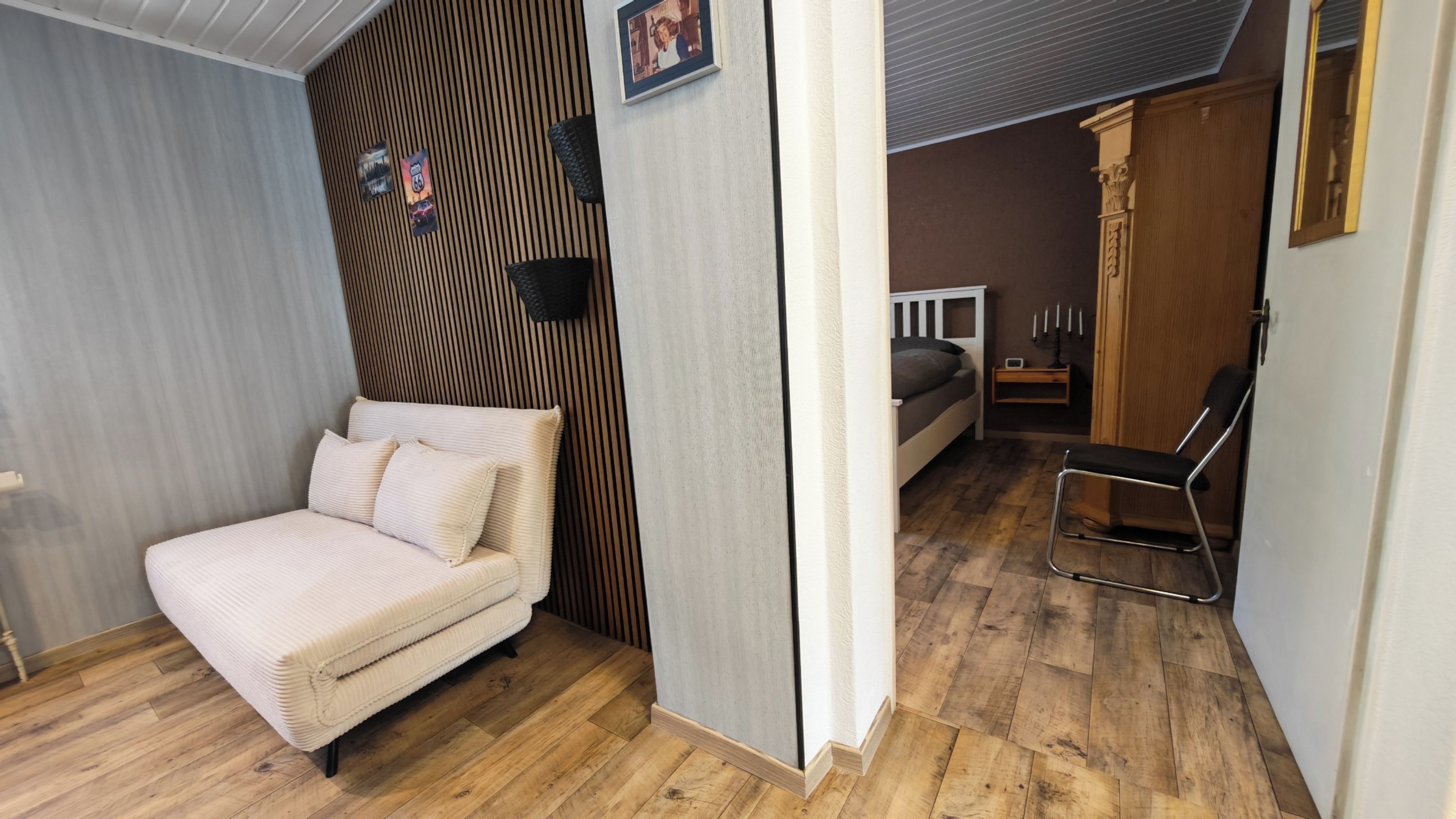 Ein Zimmer mit einem Bett, einem Sessel, Holzboden und einer Wand mit einer vertikalen Holzwandverkleidung.