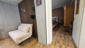 A room with a bed, a chair, a wooden floor, and a wall with a vertical wooden panel.