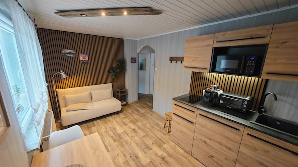 A modern kitchen with wooden cabinets, a built-in microwave, and a small dining area with a table and bench.