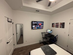 A bedroom with a bed, a desk with a computer, a TV mounted on the wall, and a mirror. - Spacious brand-new Home. Just 5 min away from Harlingen International Airport. (Harlingen)