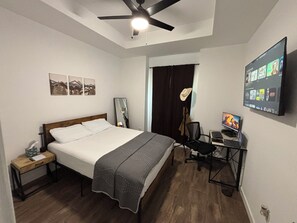 Een hotelkamer met een bed, een bureau met een computer, een televisie en een plafondventilator.