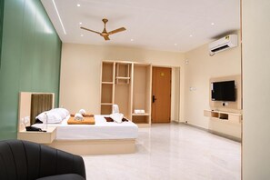 Quarto de hotel com cama, televisão, guarda-roupa, ventoinha no teto e ar condicionado.