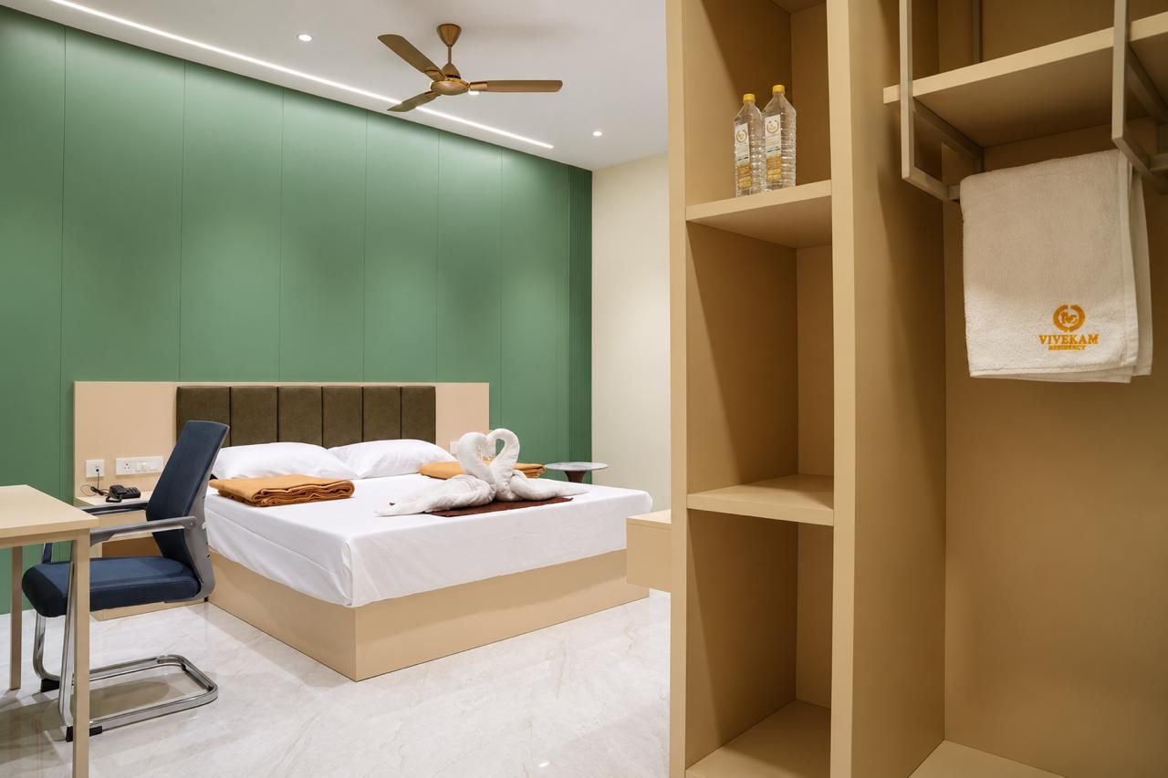 A hotel room with a bed, a desk, a chair, a wardrobe, and a ceiling fan.