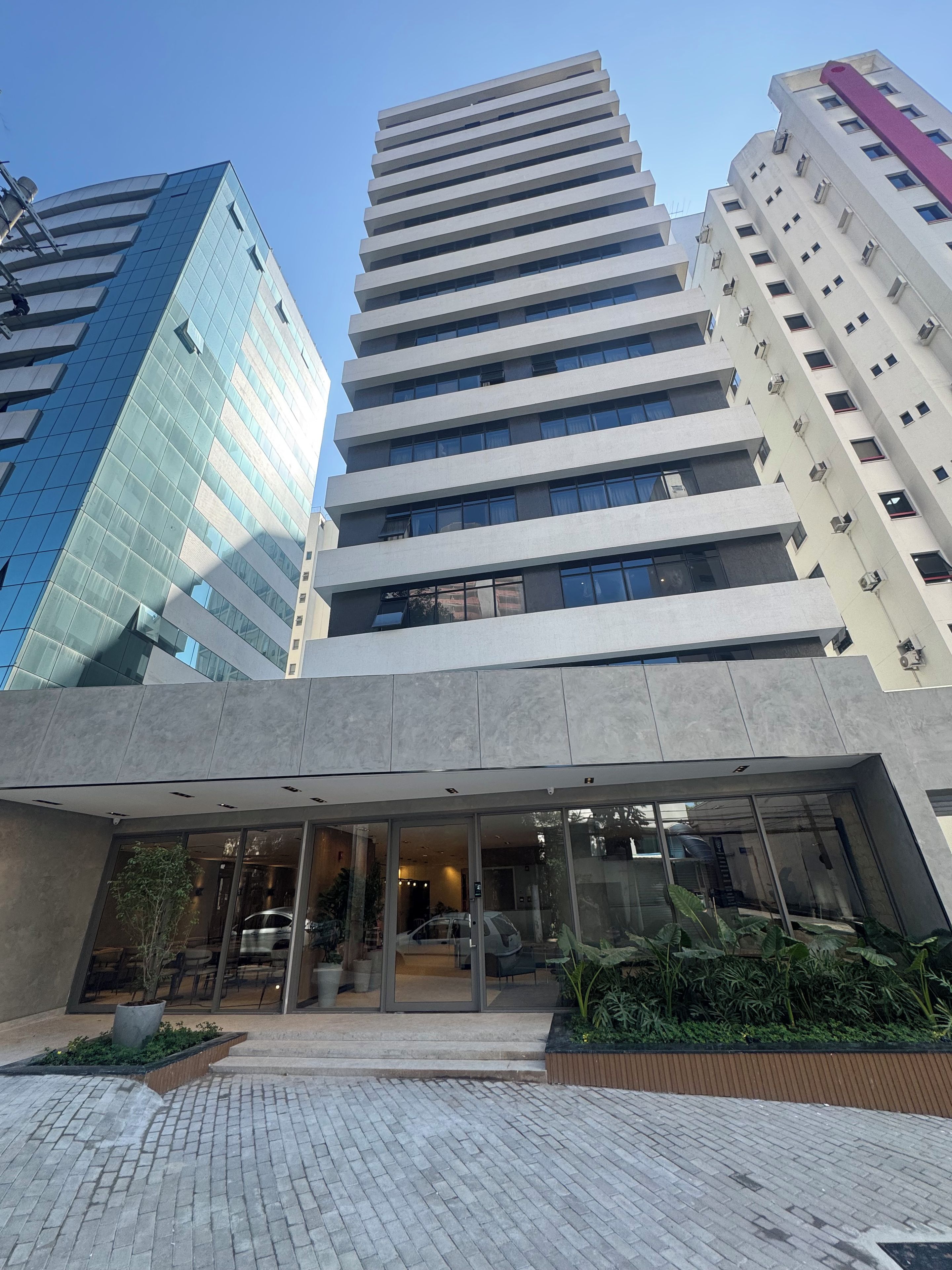 A modern building with a glass facade and a flat roof, surrounded by other high-rise buildings.