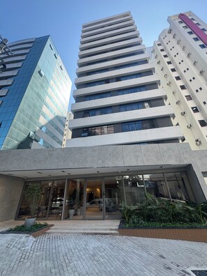 A modern building with a glass facade and a flat roof, surrounded by other high-rise buildings.
