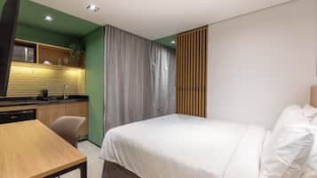 Una habitación de hotel moderna con cama, escritorio, kitchenette y baño.
