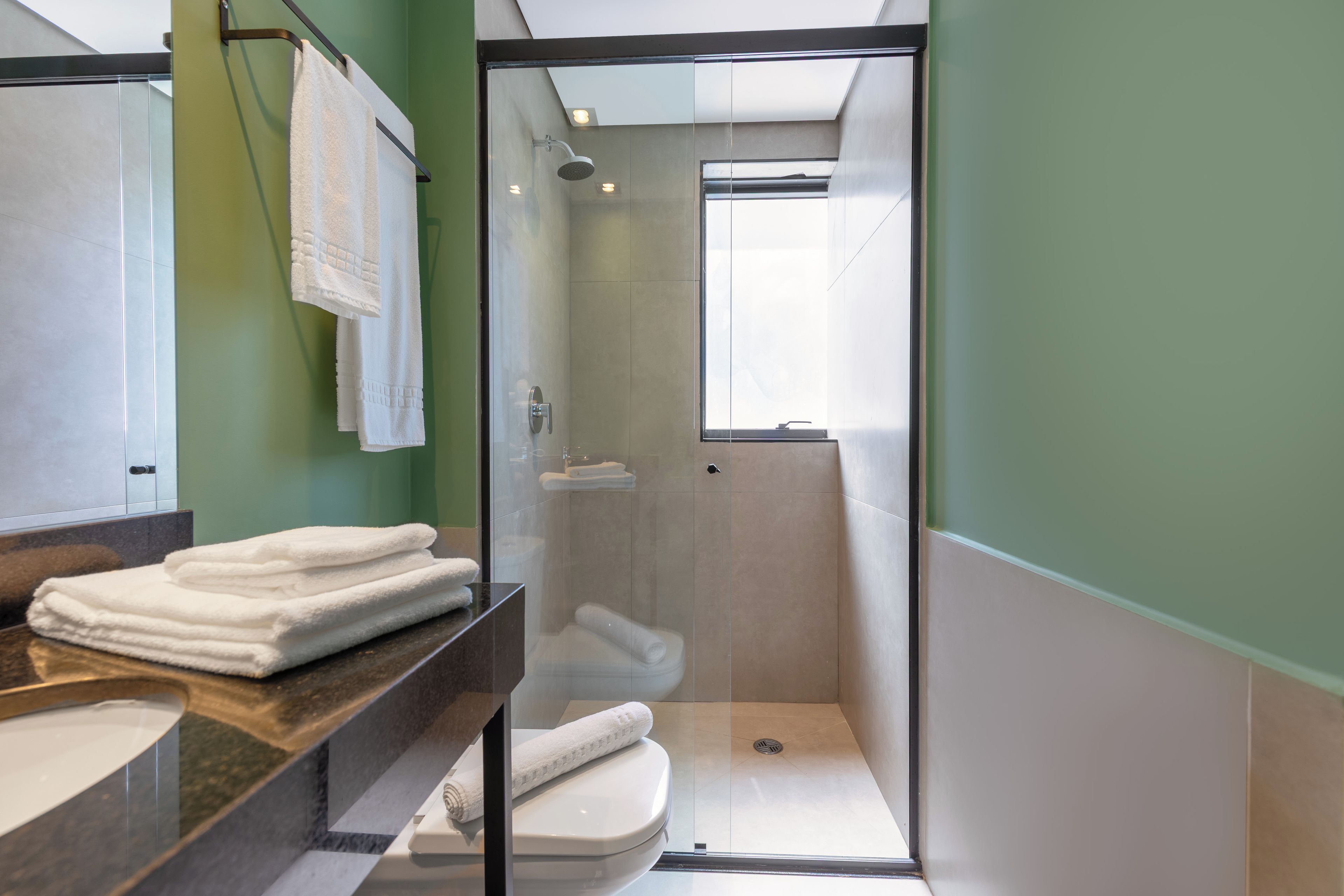 A modern bathroom with a glass-enclosed shower, a toilet, and a sink with stacked towels.