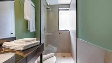 Un baño moderno con ducha envuelta en vidrio, inodoro y lavamanos con toallas apiladas.
