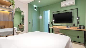 Una habitación de hotel con cama, escritorio, silla, espejo y aire acondicionado.