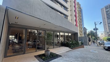 A modern building with a glass facade, outdoor seating area, and a paved walkway.