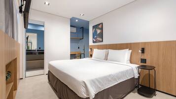 A modern hotel room with a large bed, a bedside table, a chair, and a small desk area.