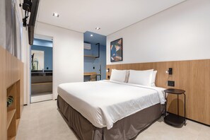 A modern hotel room with a large bed, a bedside table, a chair, and a small desk area.