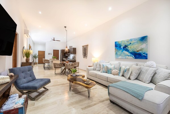 Een moderne woonkamer met een bank, fauteuil, salontafel en een eethoek met stoelen en een tafel.