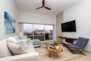 Een moderne woonkamer met een bank, fauteuil, salontafel en een aan de muur bevestigde televisie.