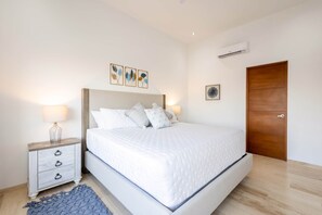 A bedroom with a bed, bedside tables, a nightstand, a wooden door, and wall-mounted artwork. - Casa Sirenas (Cabo San Lucas)