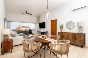 Ein modernes Wohnzimmer mit Essbereich, großen Fenstern, einem Deckenventilator und einem an der Wand montierten Flachbildfernseher.