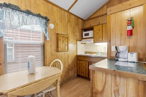 A wooden interior with a kitchen area, a dining table, and a window with blinds. - One Room Parkview Cabin - Sleeps 2 to 4 guests. (Gore)