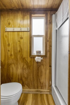 Ein kleines Badezimmer mit Holzvertäfelung, einer Toilette, einem Fenster und einem Handtuchhalter.