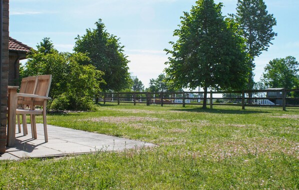 A grassy outdoor area with a wooden bench, a brick building, and a fenced area with trees. - Beautiful apartment in Ribnitz-Damgarten with WiFi (Ribnitz-Damgarten)