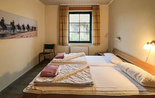 Ein Hotelzimmer mit zwei Betten, einem Sessel, einem Heizkörper, einem Fenster mit Vorhängen und einem Bild an der Wand.