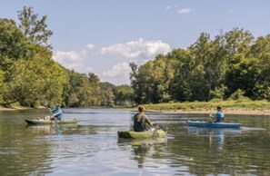 Une scène de rivière avec trois kayaks, dont un au premier plan et deux à l’arrière-plan, le tout entouré d’arbres.