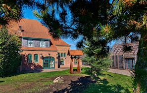 Ein traditionelles Backsteingebäude mit rotem Ziegeldach, einer Holzveranda und einem kleinen Baum im Vordergrund.