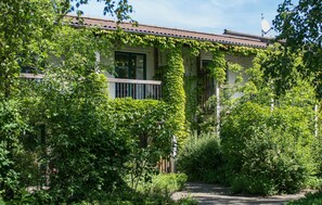 Un edificio con tejado de baldosas, rodeado de abundante vegetación y un camino que conduce a la entrada.