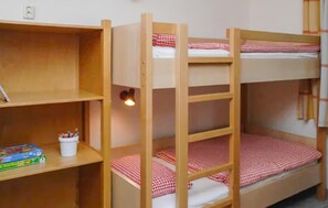 Una cama litera con una estantería a un lado, que contiene una taza y un juego de mesa.
