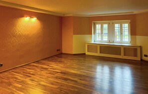 Ein Zimmer mit Holzdielenboden, einem Fenster mit Jalousien und einer an der Wand befestigten Leuchte.