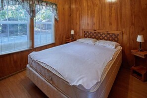 Ein Schlafzimmer mit Holzwänden, einem großen Bett, zwei Nachttischen mit Lampen und einem Fenster mit Jalousien.