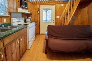 Eine kleine Küche mit Herd, Mikrowelle und Spüle. Ein braunes Sofa steht neben einer Tür mit Fenster.