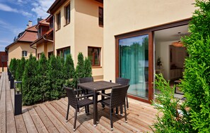 A wooden deck with a table and chairs, surrounded by evergreen shrubs, leading to a glass door entrance. - 40 - Ferienwohn Sissi & Franzl (Kuhlen-Wendorf)