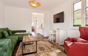 A living room with a green sofa, a red chair, a wooden coffee table, and a TV mounted on the wall. - 40 - Ferienwohn Sissi & Franzl (Kuhlen-Wendorf)