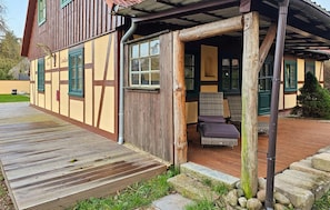 Ein traditionelles Gebäude mit einer Holzterrasse, einer Veranda und einem Kiesweg, der zum Eingang führt.