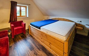 A bedroom with a wooden bed, a red chair, a window with curtains, and a wooden floor. - 45 - Ferienhaus Landlust (Kuhlen-Wendorf)