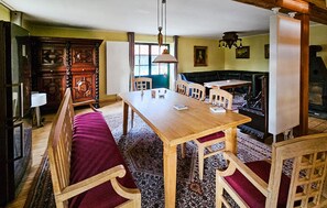 A dining area with a wooden table and benches, a fireplace, and a window with curtains. - 45 - Ferienhaus Landlust (Kuhlen-Wendorf)