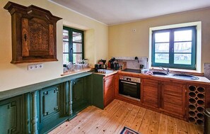 A kitchen with wooden cabinets, a built-in oven, and a large window. - 45 - Ferienhaus Landlust (Kuhlen-Wendorf)