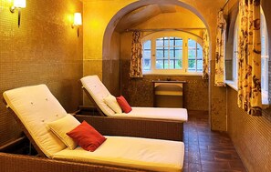 Ein Spa-Raum mit zwei Liegestühlen, einem kleinen Waschbecken und einem Fenster mit Vorhängen.