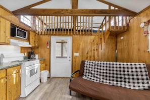 Eine kompakte Küche mit Herd, Mikrowelle und Schränken, eine Holztreppe sowie eine Couch mit kariertem Überwurf.