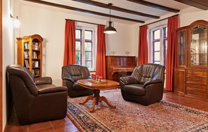 Ein Zimmer mit Ledersesseln, einem Holztisch, einem Klavier und einem Bücherregal.