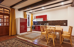 A modern kitchen with red cabinets, a dining table with chairs, and a patterned rug. - 48 - Ferienhaus XL Oliver (Kuhlen-Wendorf)