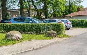Ein Parkplatz mit Autos, einem gepflasterten Weg und einer Hecke.