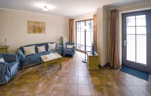 Ein Wohnzimmer mit einer Couch, einem Couchtisch, einem Fernseher und einem großen Fenster mit Vorhängen.