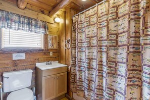 Ein Badezimmer einer Holzhütte mit Toilette, Waschbecken und einer Duschvorhang mit Angelködern.