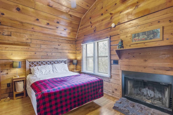 Ein Schlafzimmer einer Holzhütte mit Bett, Kamin und einem Fenster mit Jalousien.