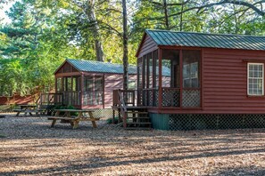 Eine Hütte mit Veranda, Deck und Picknicktisch in einem bewaldeten Gebiet.