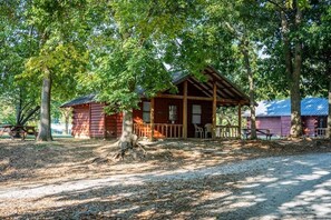 A rustic cabin with a porch, surrounded by trees. - Deluxe Cabin Studio - Sleeps up to 8 guests. (Gore)