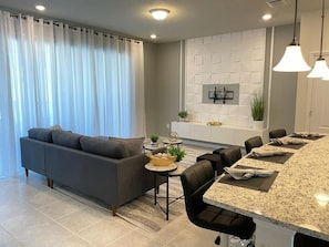 Ein modernes Wohnzimmer mit einer Couch, Essbereich, Kücheninsel und Pendelleuchten.