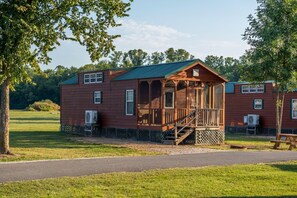 A wooden cabin with a porch, a fenced yard, and a picnic table. - Double Deluxe Cabin - Sleeps 8 to 10 guests. (Gore)